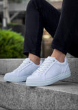 White sneakers worn on a person sitting on concrete steps with a blurred green background